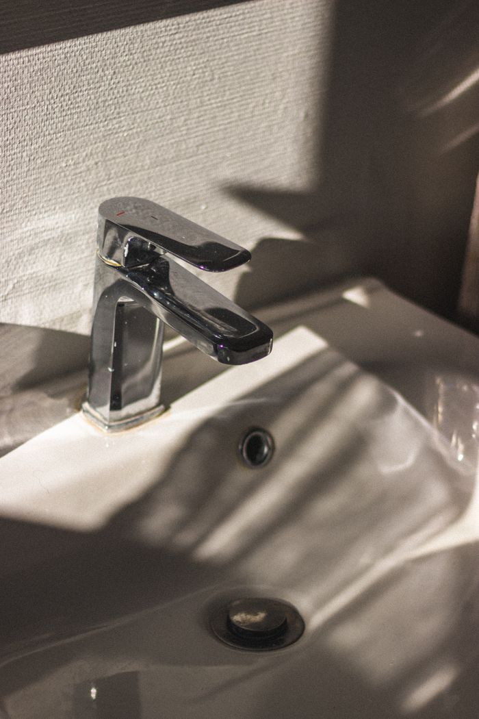 hero-img-02 Closeup of chrome single handle faucet installed on white ceramic sink in bathroom at sunlight